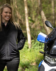a blong smiling woman standing by her big motorcycle wearing a black mesh motorcycle jacket for women