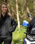 a blong smiling woman standing by her big motorcycle wearing a black mesh motorcycle jacket for women