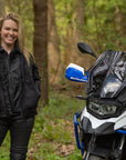 a blong smiling woman standing by her big motorcycle wearing a black mesh motorcycle jacket for women