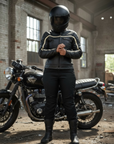 Person wearing a black motorcycle helmet and jacket standing next to a motorcycle in an industrial setting.