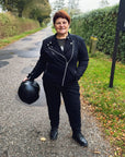 a smiling red haired woman motorcyclist wearing witches of wheels t-shirt, black jeans and mc jacket