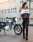 A woman wearing black leather boots and Triumph shirt walking away from her motorcycle