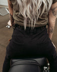 a back of a woman siting on a motorcycle wearing adjustable waist black mc pants