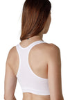 The back of a dark-haired woman wearing a white sport bra with wide straps from Tremonte.