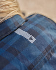 Close-up of a person wearing a blue plaid shirt with a brand logo SHIMA on the chest.
