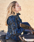Woman in a blue plaid jacket sitting on a motorcycle in a desert setting