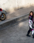 Young woman wearing black, white, pink SHIMA motorcycle leather suit with her red motorcycle