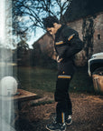 Person wearing a black tracksuit with yellow stripes outdoors near a building.