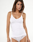 Dark-haired woman wearing a white sleeveless tank top with bow detail and matching thongs with lace details from Tramonte.