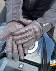 Person wearing brown gloves on a motorcycle, with a focus on the gloves and motorcycle.