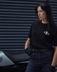 A young woman standing by her motorcycle wearing blue high waist motorcycle jeans and pando moto t-shirt