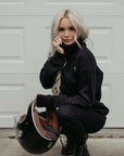 A young blond women wearing high neck black sweatshirt with motogirl logo in front