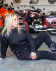 A blong woman sitting on the floor by motorcycles wearing women's motorcycle jacket from Moto Girl