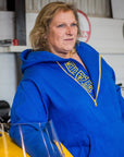 A blond woman standing by a motorcycle wearing blue and yellow motorcycle hoodie from Moto Girl
