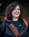 A smiling woman wearing Black and orange motorcycle hoodie from MotoGirl with a long zip