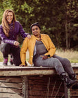 two smiling women sitting outside wearing a mustard yellow and purple Valerie leather jacket from moto girl