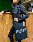 A woman leaning on the shop counter wearing black women's garage suit from MotoGirl and a MotoGirl bag