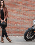 A young woman by a motorcycle wearing brown motorcycle leather jacket and brown women motorcycle boots from Shima