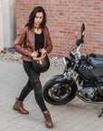A young woman by a motorcycle wearing brown motorcycle leather jacket and brown women motorcycle boots from Shima