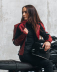 A young woman on her motorcycle wearing a red and black women's motorcycle jacket with reflectors on the sleeves.
