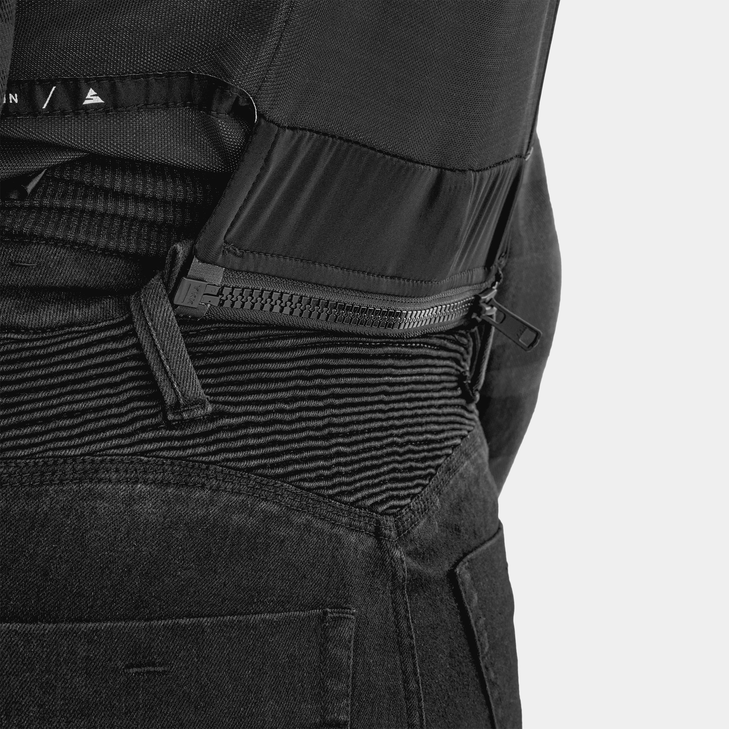 Close-up of a black tactical backpack with multiple zippers and straps on a light gray background.