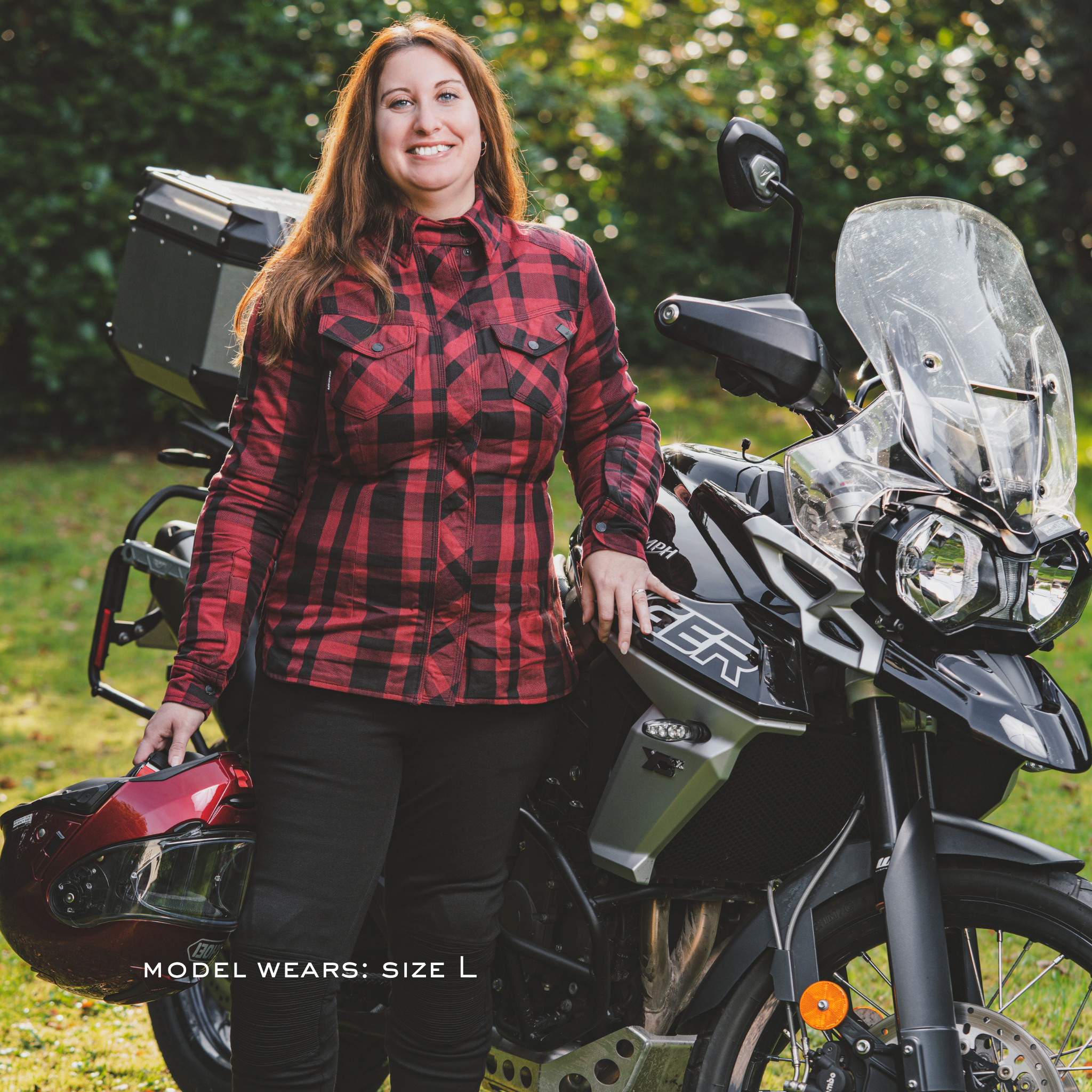 Woman in a red and black plaid SHIMA renegade motorcycle shirt standing next to a motorcycle with a helmet.