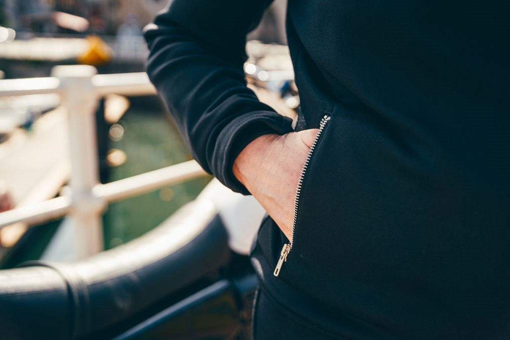 Person wearing a black jacket with a zipper, standing on a bridge.