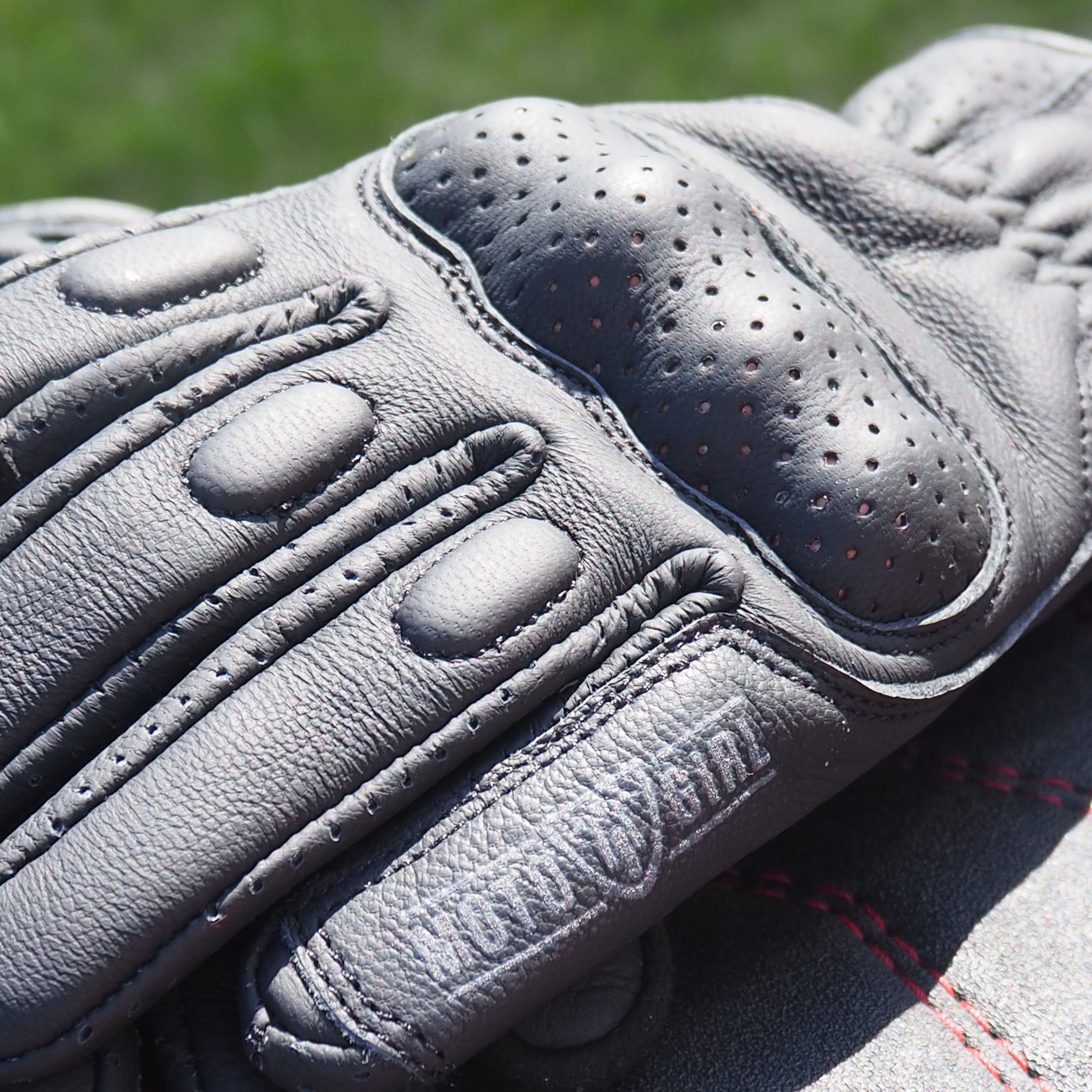 Gray leather glove with red stitching on a blurred grass background