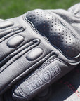 Gray leather glove with red stitching on a blurred grass background