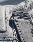 Close-up of a gray leather glove with a MotoGirl brand logo on a blurred background