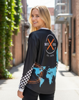 Woman wearing a black long-sleeve shirt with a world map design, standing in an alleyway.