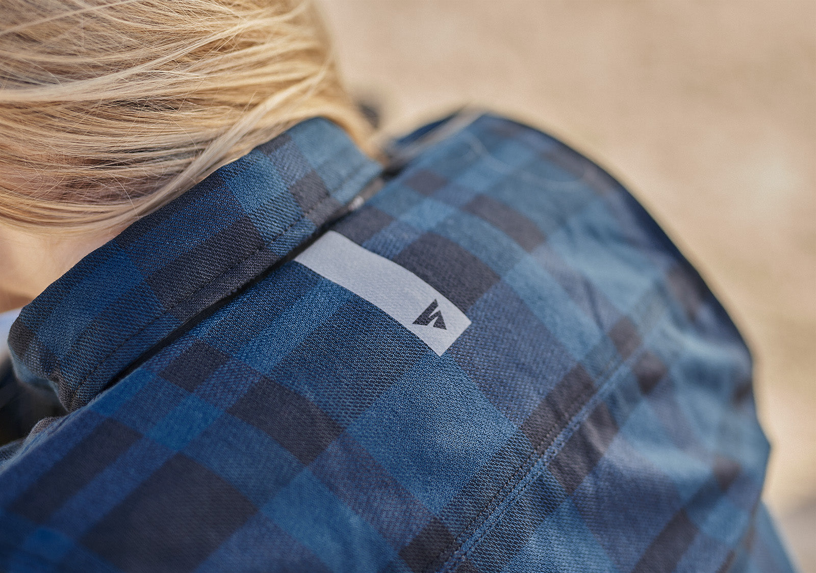 Close-up of a person wearing a blue plaid shirt with a brand logo  SHIMA on the chest.
