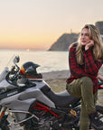 Woman sitting on a Ducati motorcycle by a body of water at sunset