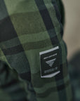 Green plaid fabric with a brand logo tag on a blurred background