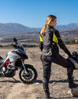 A woman standing by her motorcycle wearing Black SHIMA touring motorcycle pants for women