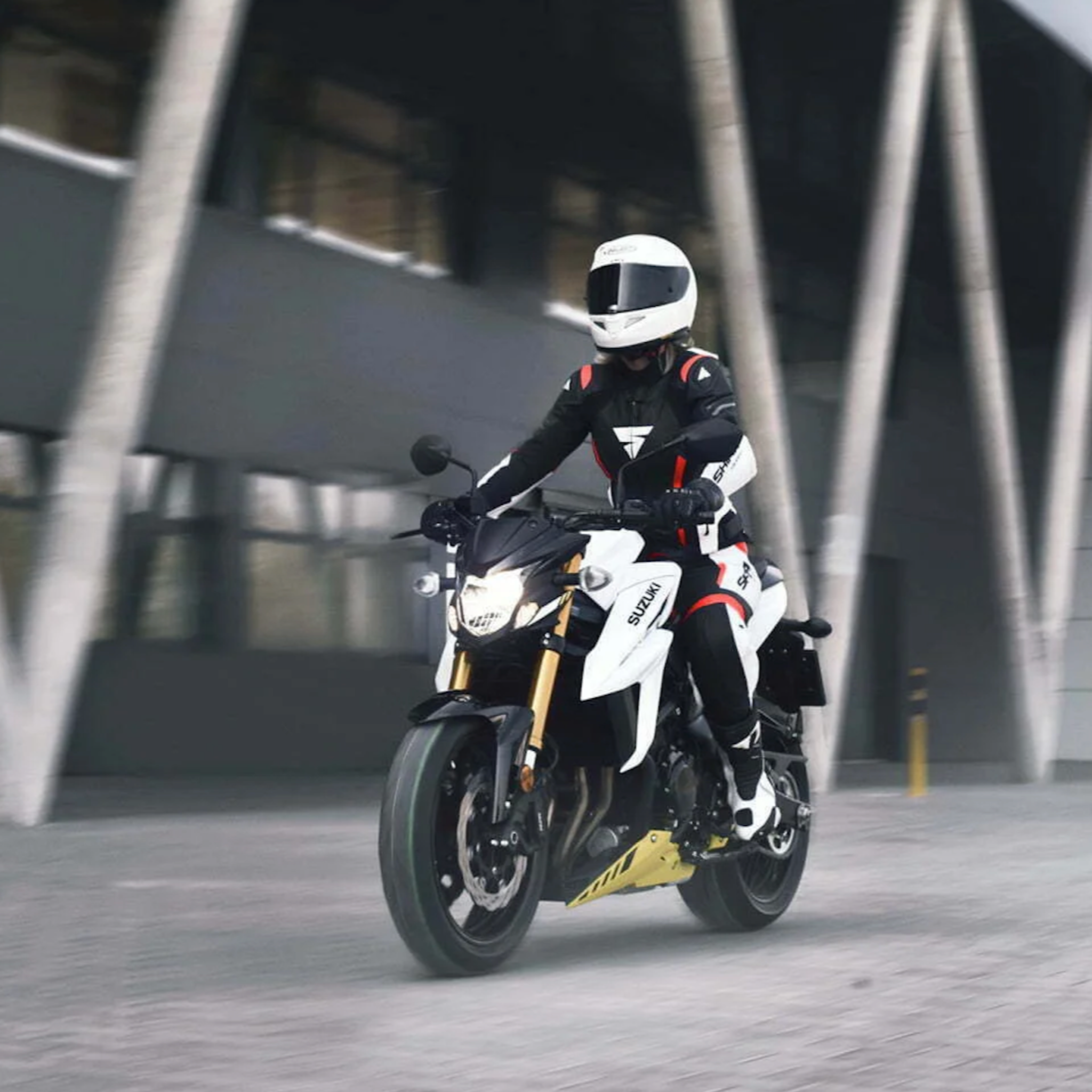 A woman on a white Suzuki motorcycle wearing SHIMA MOTORCYCLE LEATHER suit IN BLACK FLUO, WHITE AND RED FLUO