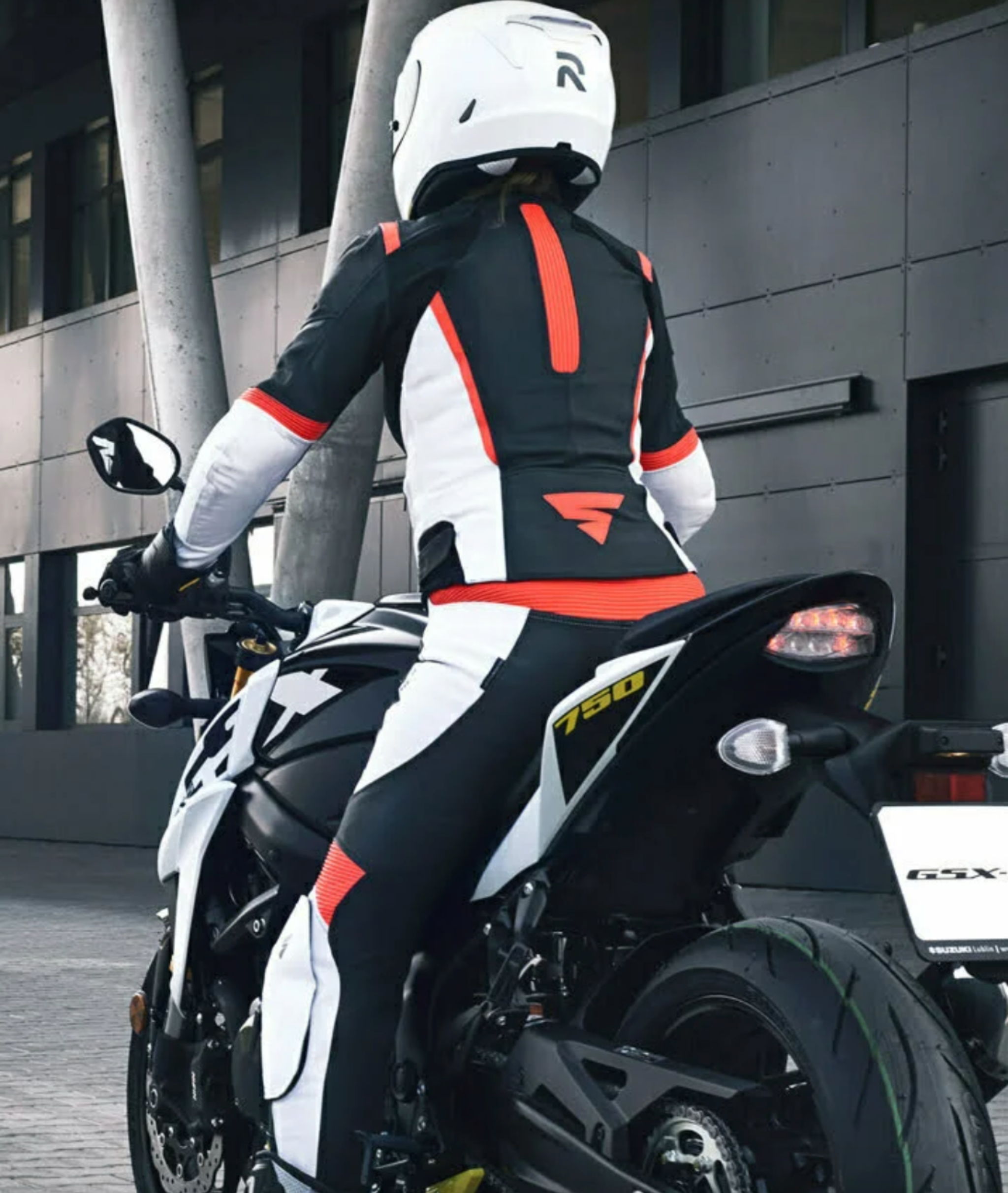 A woman on a motorcycle wearing SHIMA MOTORCYCLE LEATHER suit IN BLACK FLUO, WHITE AND RED FLUO