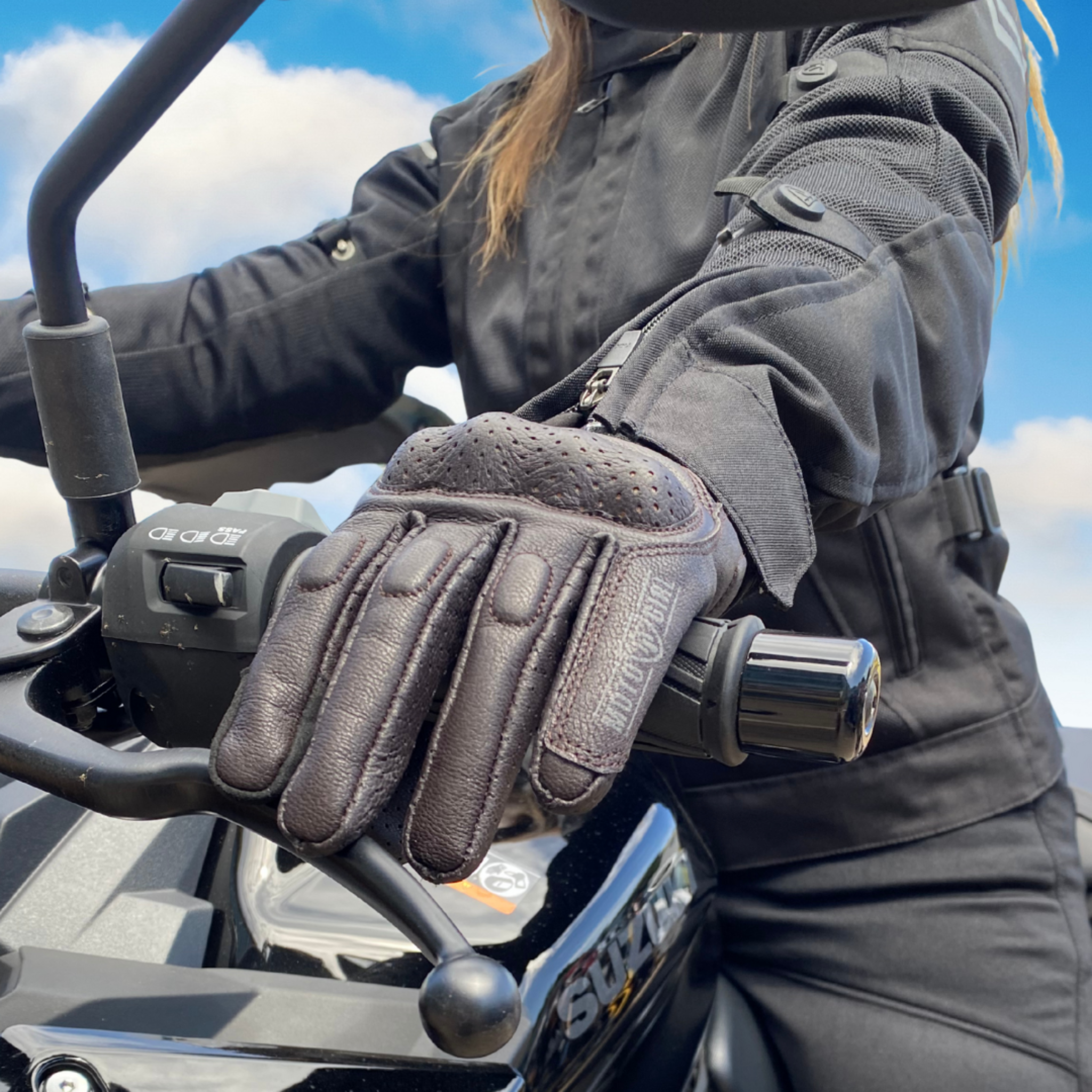 Person wearing a black glove on a motorcycle with a blue sky background
