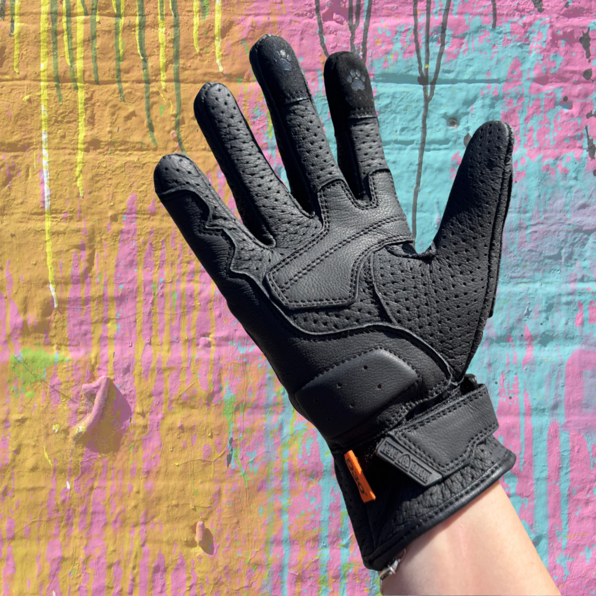 Black glove on a hand against a colorful, textured background