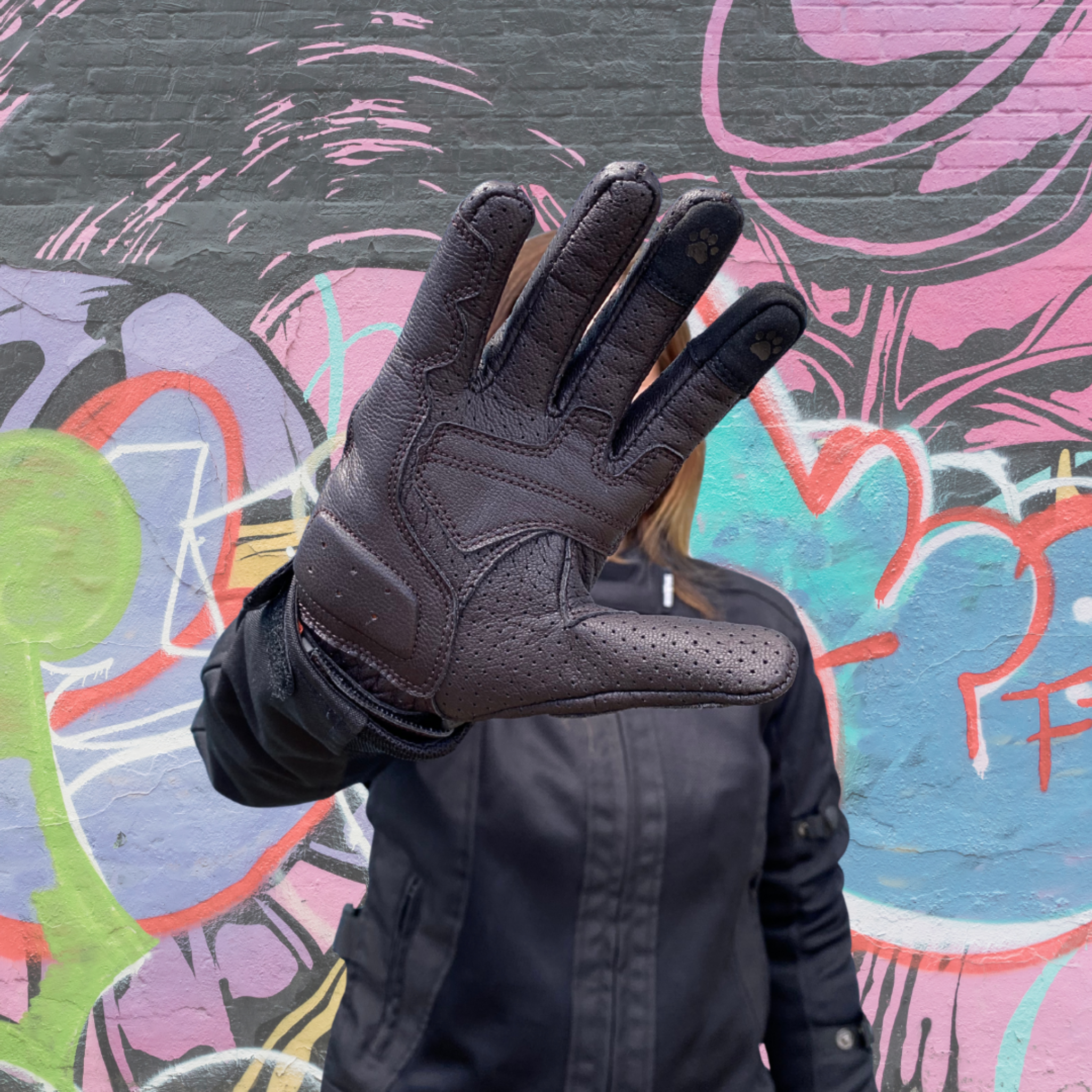 Person wearing a black glove against a colorful graffiti wall.