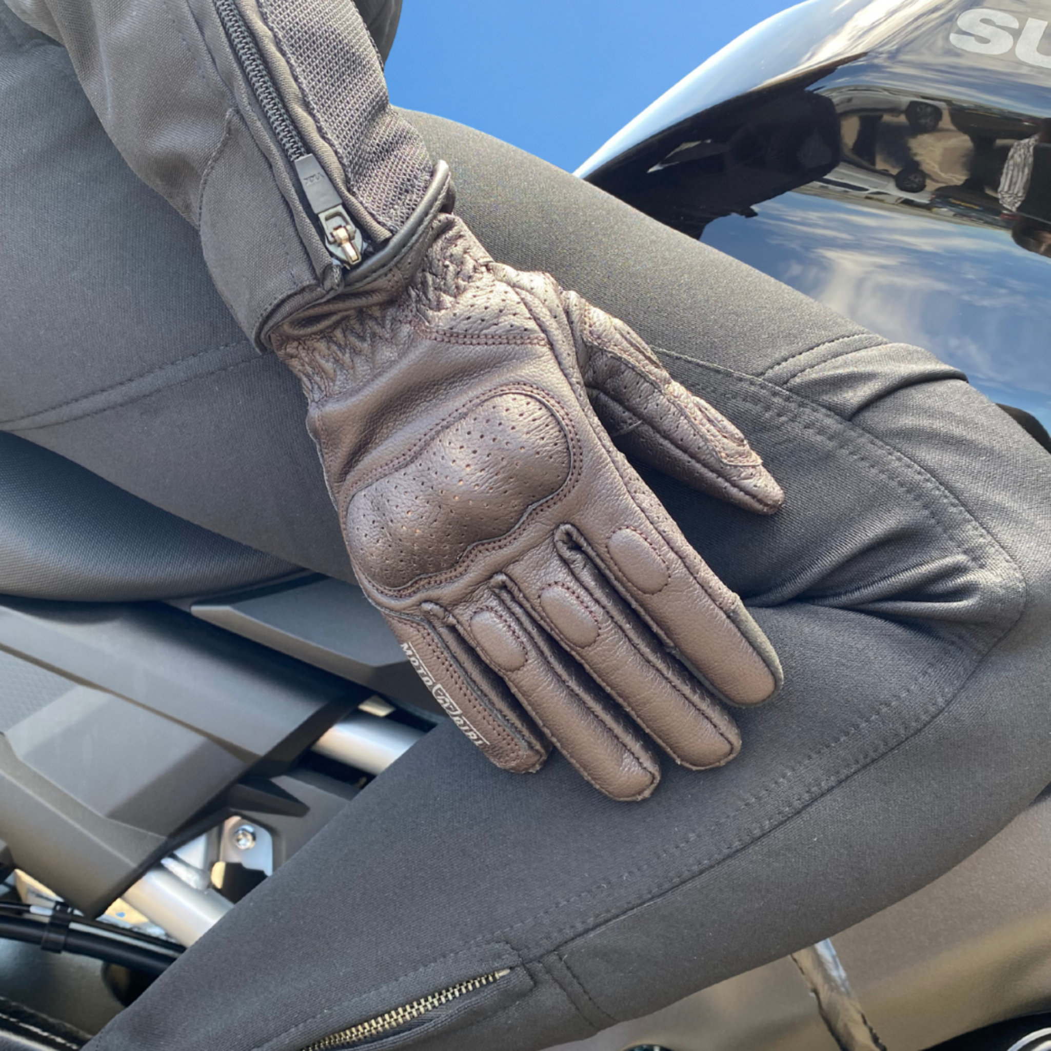 Beige motorcycle glove on a person sitting on a motorcycle with a clear blue sky background