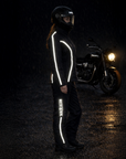 Person wearing a reflective motorcycle suit standing next to a motorcycle in a dark setting.