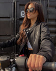 a young lady on a motorcycle wearing Black retro style woman's motorcycle jacket with silver zip details