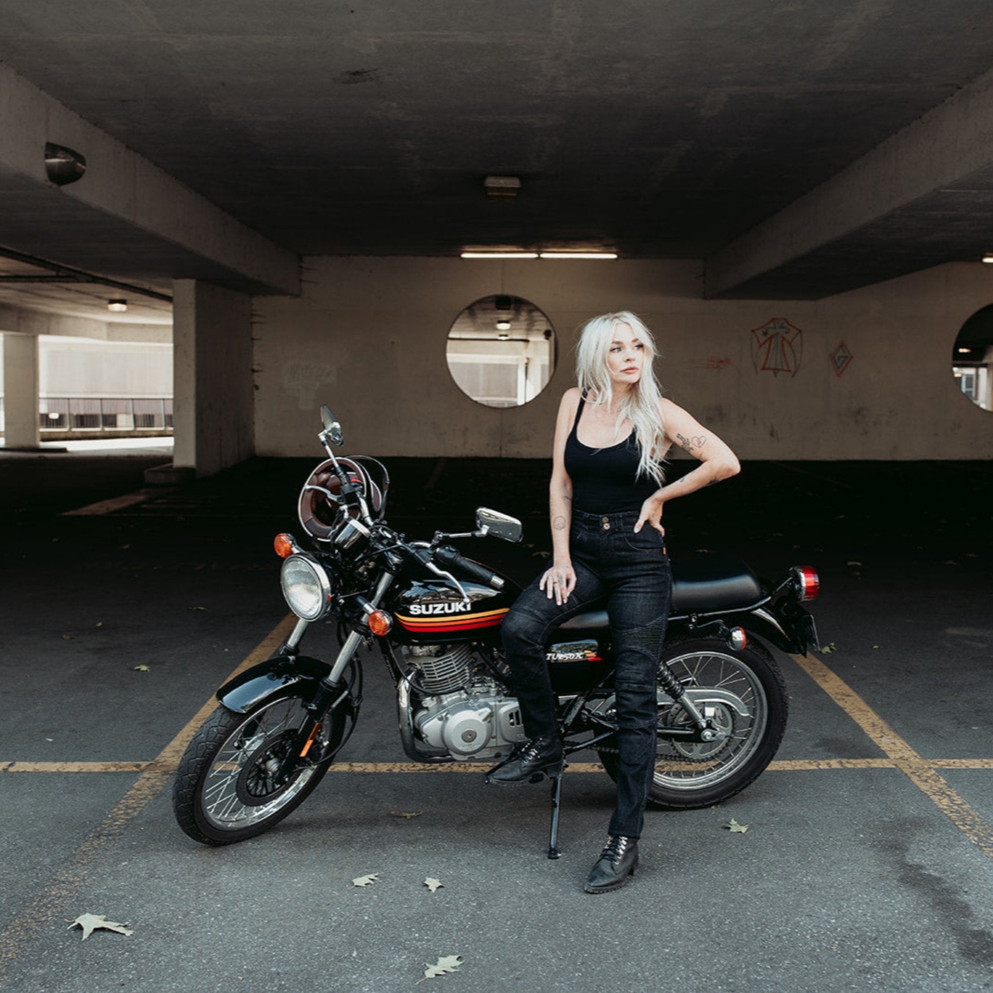 A tattooed woman on her Suzuki motorcycle wearing black lady motorcycle jeans from Moto Girl.