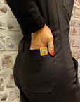 A close up of a woman holding her hand in the back pocket of black women's garage jumpsuit from MotoGirl