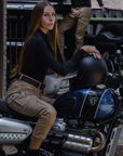 a brunette woman sitting on her motorcycle wearing beige mc pants 