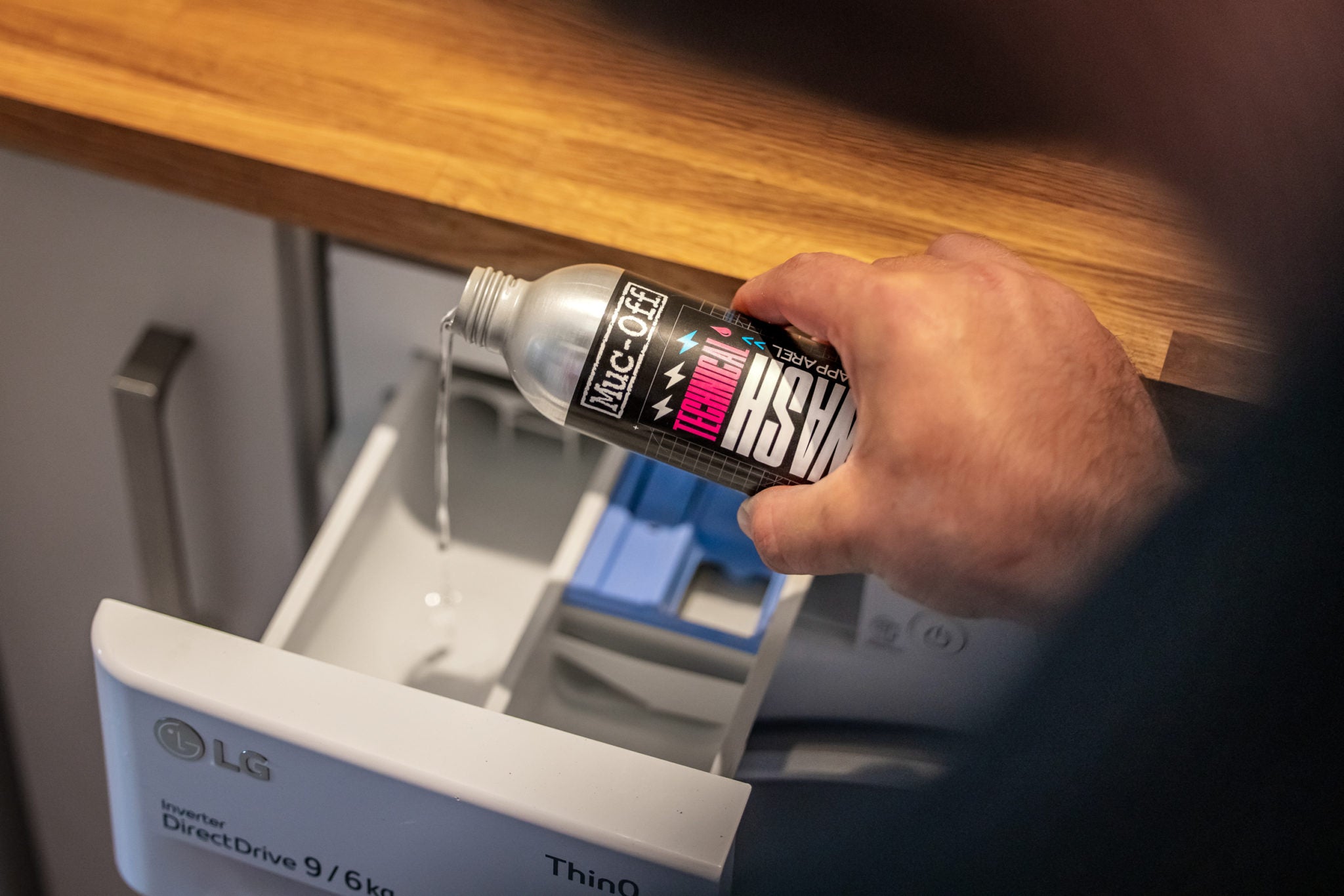 A Muc-off technical wash for motorcycle clothes is being poured into the washing machine