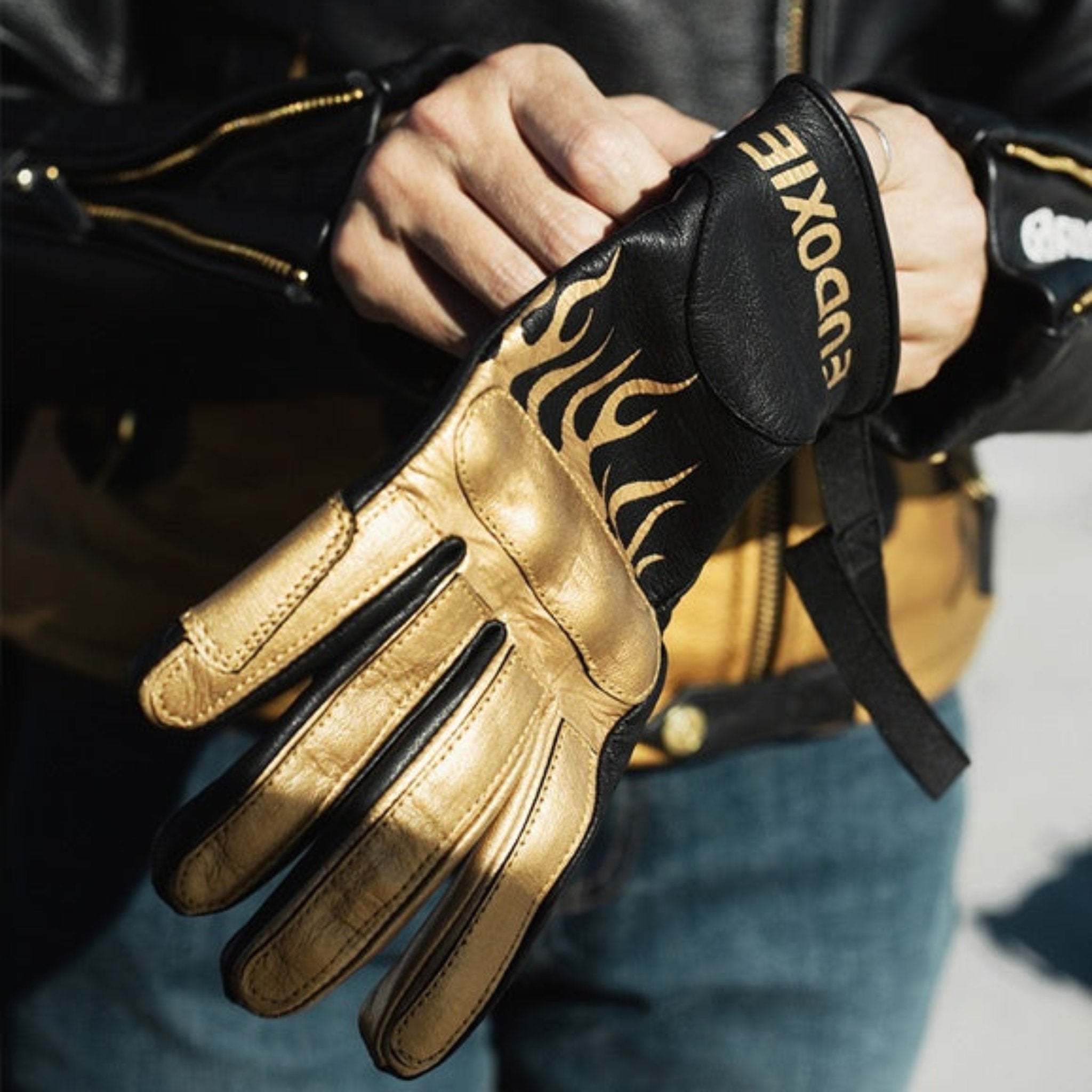 woman's hands putting on a black Eudoxie mc glove with golden flames 