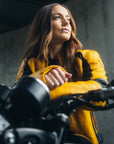 A young woman on her motorcycle wearing a yellow and black women's motorcycle jacket.